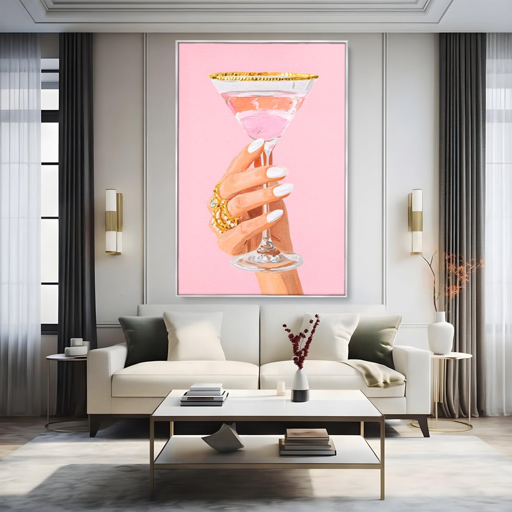 Tablou canvas cu ilustratie cu mana care tine pahar de cocktail, in rama de aluminiu argintiu, pe perete intr-un living